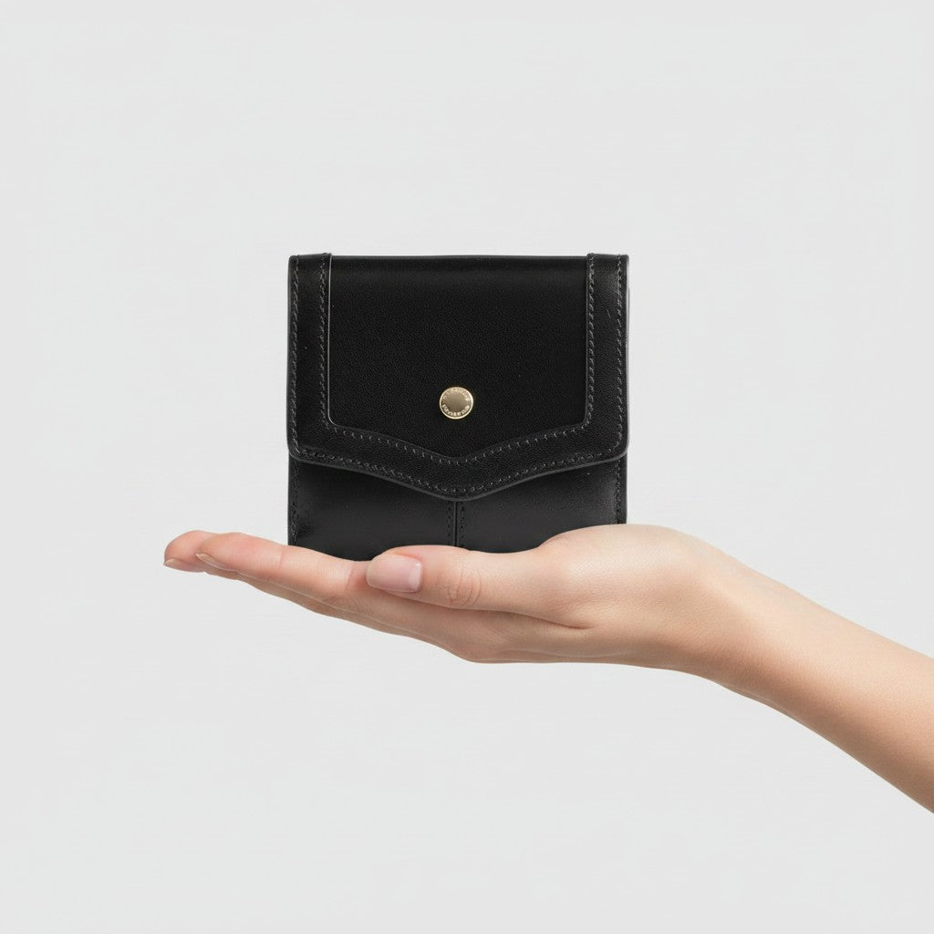 Portafoglio donna LIBUTTI The Bridge linea Agnese in pelle nera con bottone oro, tenuto nel palmo di una mano