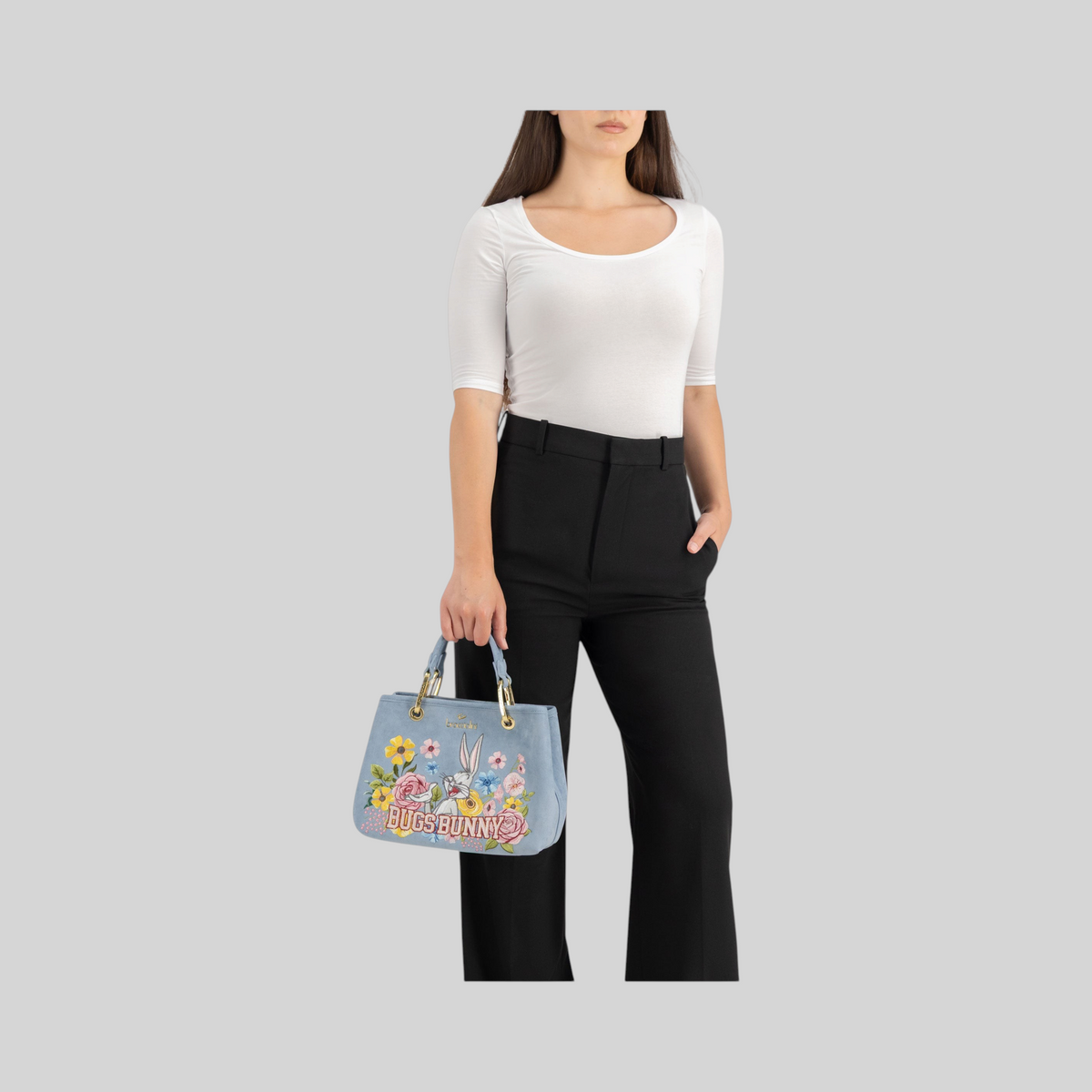 Borsa a mano LIBUTTI azzurra effetto suede con ricamo floreale di Bugs Bunny e doppi manici, indossata da una modella.
