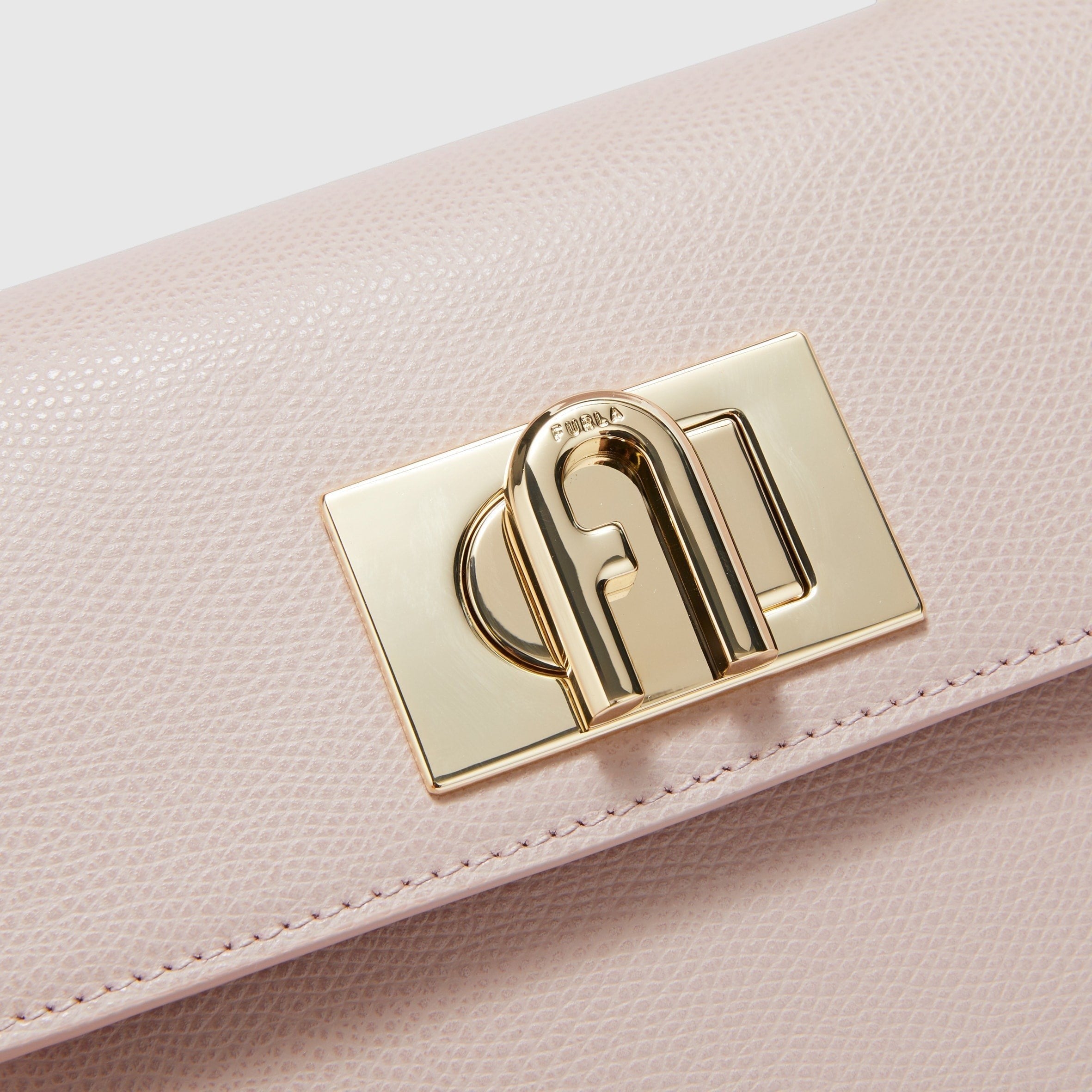 Dettaglio della chiusura a girello dorata con logo Arco su borsa mini Furla 1927 in pelle rosa di LIBUTTI